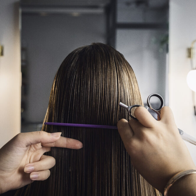 Brändikuvassa kampaaja leikkaa naisen pitkiä hiuksia.