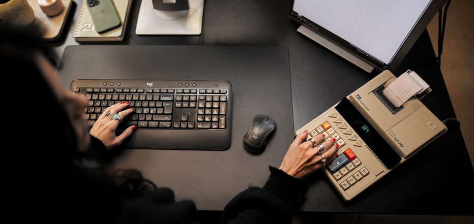 Verkkomyyntioppaan kansikuvassa yrittäjä istuu tietokoneen ääressä kädet näppäimistöllä ja laskukoneella.