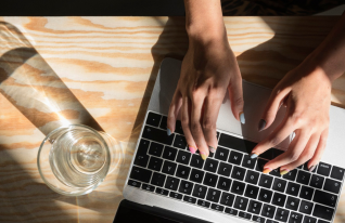 Naisen kädet kannettavan tietokoneen näppäimistöllä.