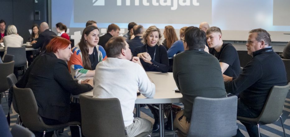 Ihmisiä tapahtumassa istumassa pöydän ympärillä