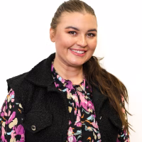 Nuori nainen hymyilee pirteässä paidassa kameralle.